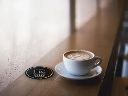 Tarjeta NFC de reseñas de Google sobre la barra de una cafetería junto a una taza de café