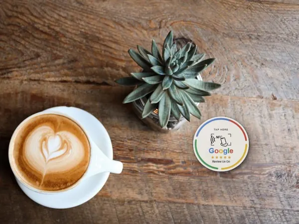 Tarjeta NFC de reseñas de Google apoyada sobre una mesa de madera junto a un café con leche