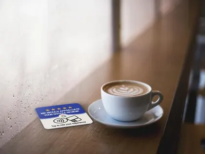 Tarjeta NFC de reseñas de Google sobre la barra de una cafetería junto a una taza de café